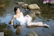 A woman in a white dress sitting on a rock in the water.