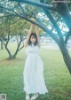 A woman in a white dress standing under a tree.