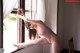 A woman in a pink leotard leaning against a window.